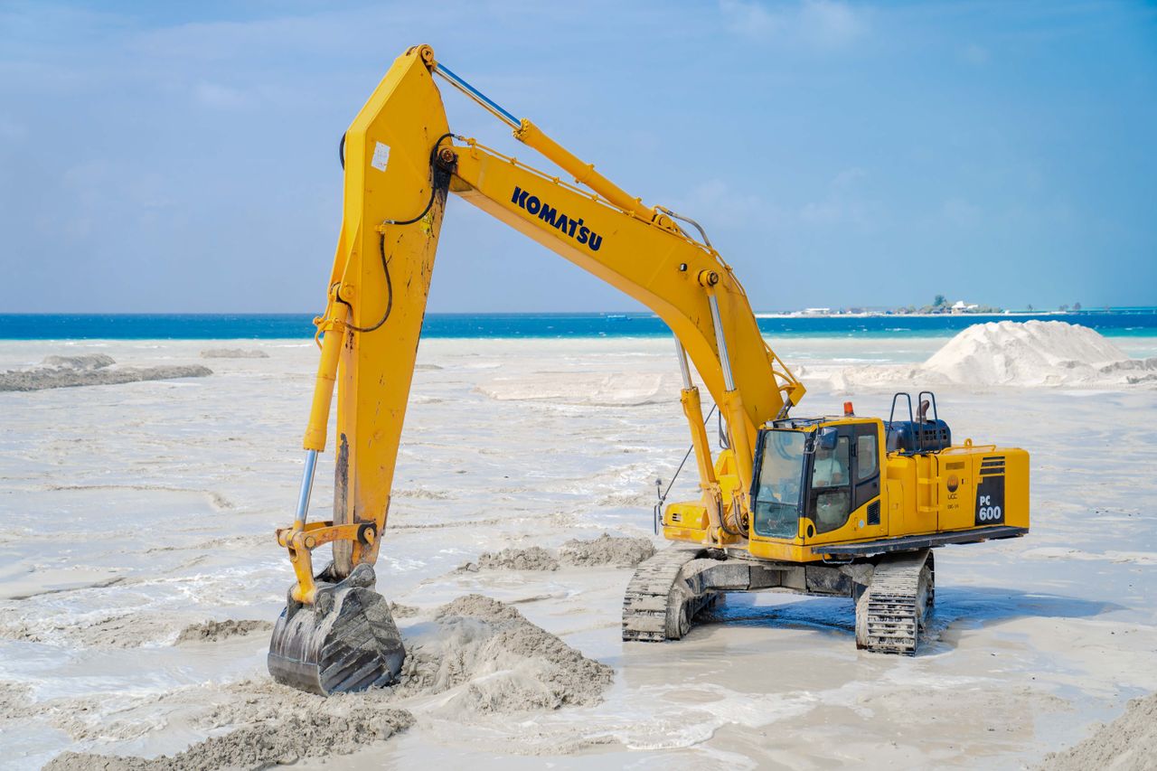 Crafting Captivating Headlines: Your awesome post title goes here A large yellow excavator operates on a coastal construction site with blue sea in the background.